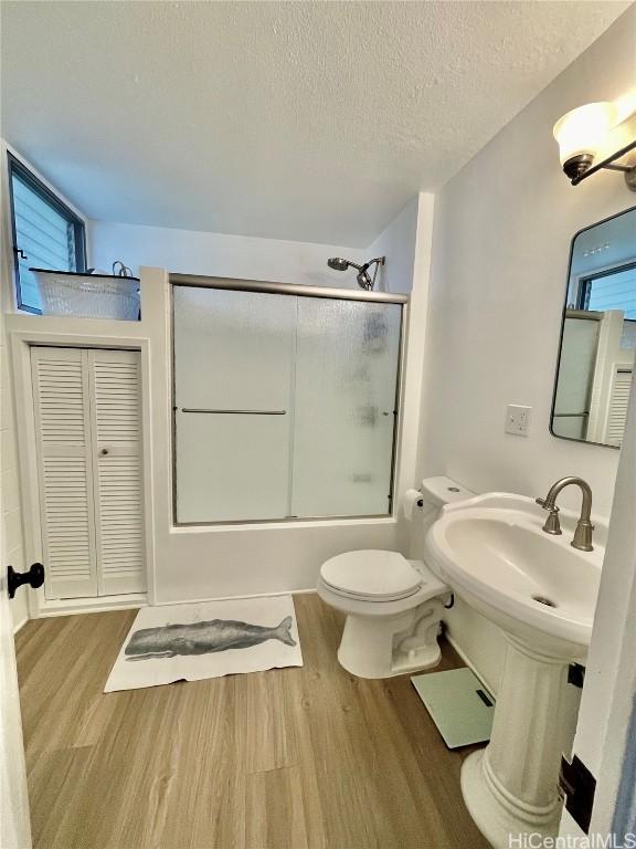 full bathroom featuring a textured ceiling, wood finished floors, shower / bath combination with glass door, and toilet