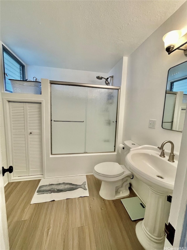 bathroom with a textured ceiling, wood finished floors, toilet, and shower / bath combination with glass door