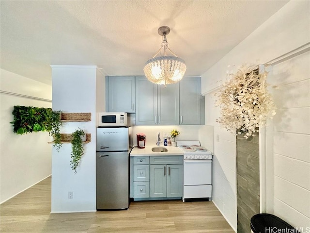 kitchen with light countertops, light wood-style flooring, a notable chandelier, white appliances, and a sink