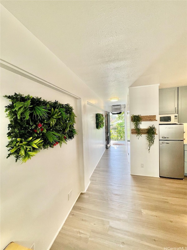 hallway with light wood-style flooring, a textured ceiling, and a wall unit AC