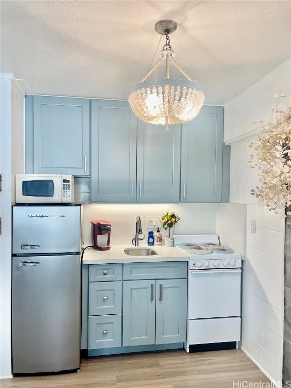 kitchen with white appliances, blue cabinetry, light wood-style flooring, a sink, and light countertops