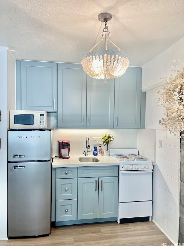 kitchen with a sink, blue cabinets, light wood-style floors, and white appliances
