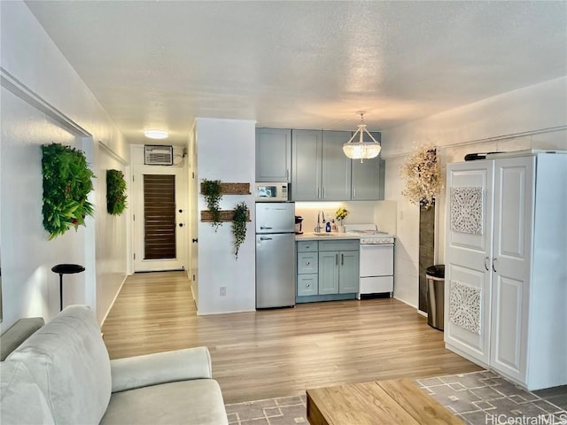 kitchen with gray cabinetry, freestanding refrigerator, light wood-style floors, light countertops, and white microwave