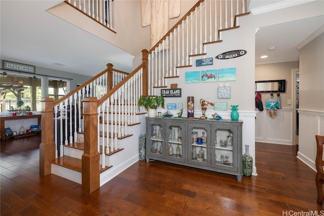 staircase with wood-type flooring, a wainscoted wall, crown molding, and a towering ceiling