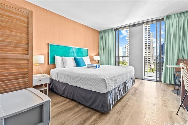 bedroom featuring access to outside, floor to ceiling windows, a city view, and wood finished floors