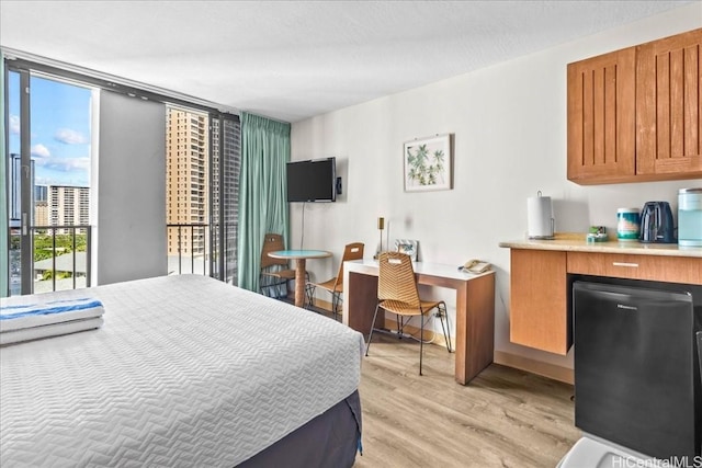 bedroom featuring floor to ceiling windows, light wood-style floors, and refrigerator