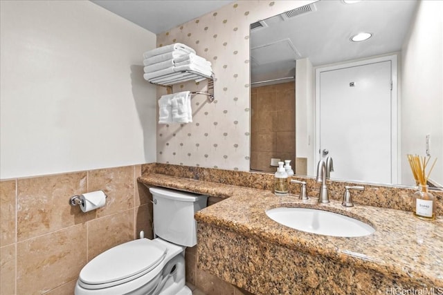 bathroom with toilet, visible vents, tile walls, wainscoting, and wallpapered walls