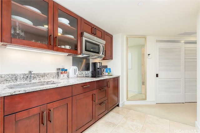 kitchen with light stone counters, stainless steel microwave, glass insert cabinets, a sink, and black electric cooktop