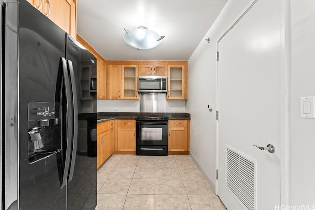 kitchen featuring light tile patterned floors, dark countertops, visible vents, glass insert cabinets, and black appliances