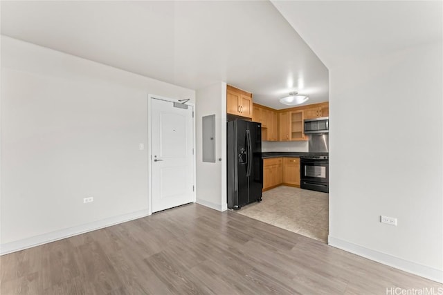 kitchen with dark countertops, stainless steel microwave, light wood-style flooring, stove, and black fridge