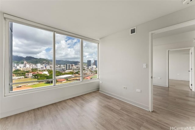 unfurnished room with a city view, wood finished floors, visible vents, and baseboards