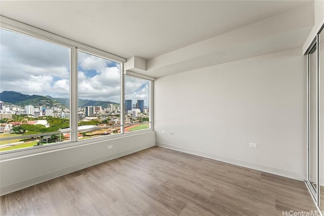 spare room with baseboards, wood finished floors, a mountain view, and a city view