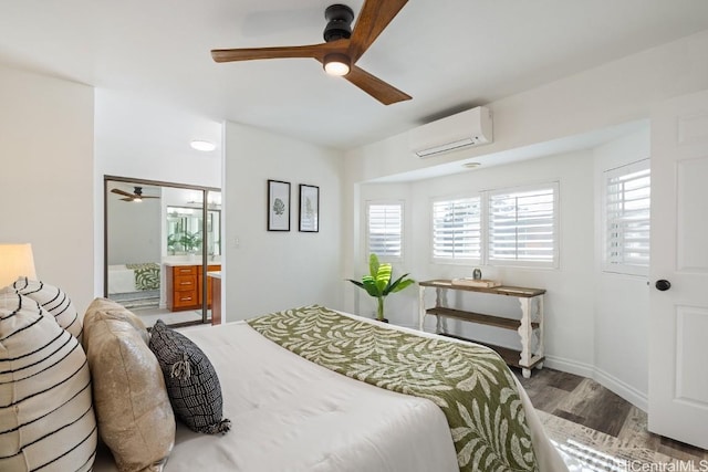 bedroom with baseboards, a ceiling fan, ensuite bath, wood finished floors, and an AC wall unit