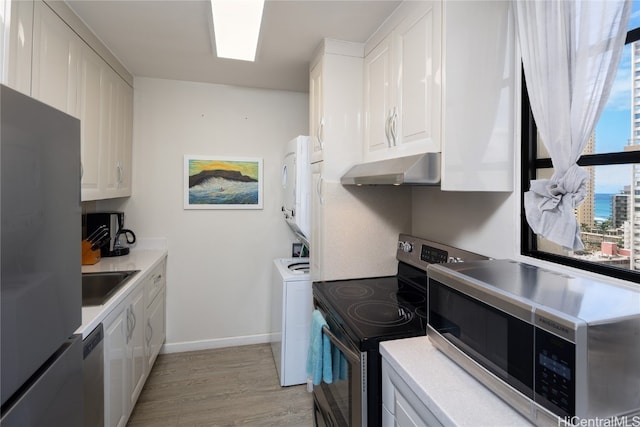 kitchen featuring under cabinet range hood, white cabinetry, stainless steel appliances, and stacked washer and dryer