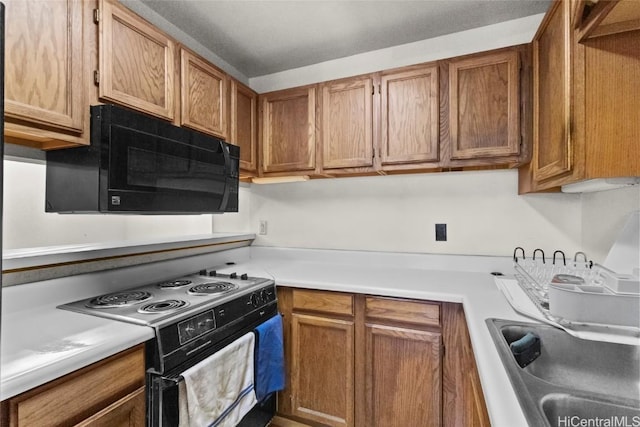 kitchen with a sink, black appliances, light countertops, and brown cabinets