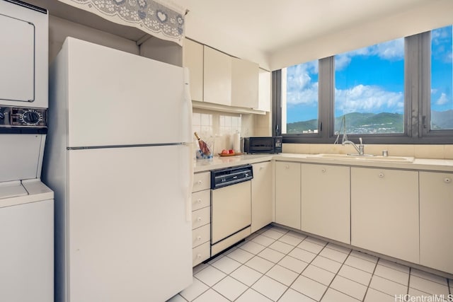 kitchen featuring white appliances, stacked washer and dryer, light countertops, a sink, and light tile patterned flooring