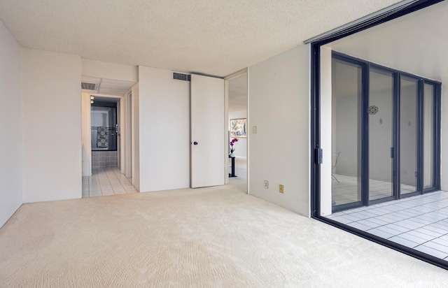 carpeted empty room with tile patterned flooring, visible vents, and a textured ceiling