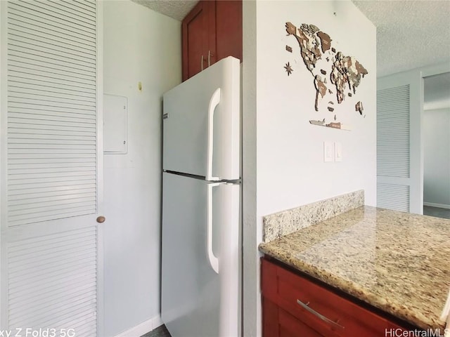 kitchen featuring light stone counters, a textured ceiling, and freestanding refrigerator