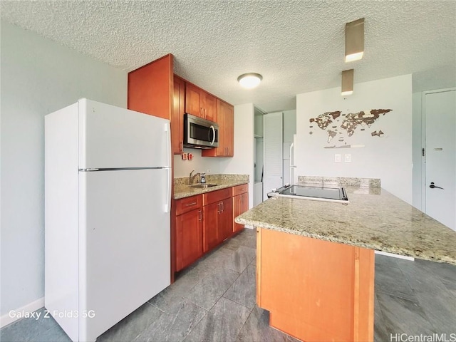 kitchen with a sink, stainless steel microwave, freestanding refrigerator, a peninsula, and range