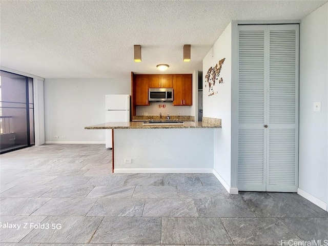 kitchen with stainless steel microwave, baseboards, brown cabinets, a peninsula, and freestanding refrigerator