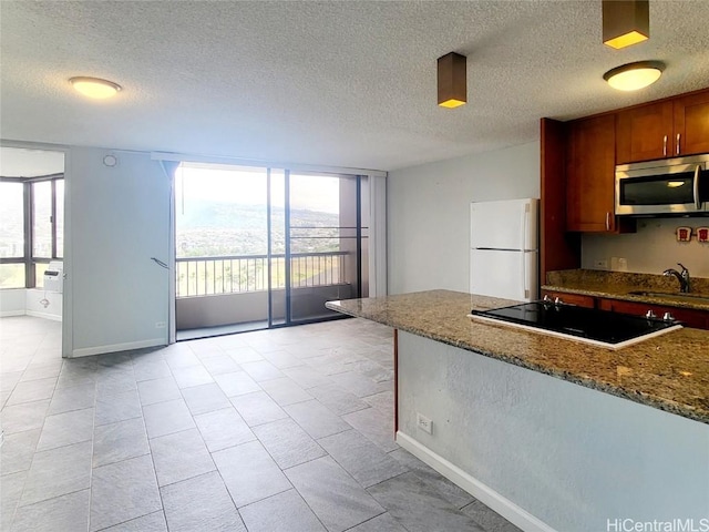 kitchen featuring a sink, stainless steel microwave, dark stone countertops, freestanding refrigerator, and black electric stovetop