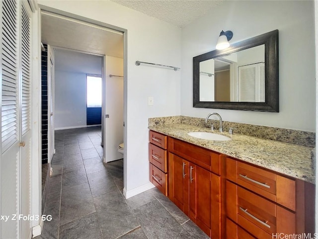 bathroom with toilet, a textured ceiling, vanity, and baseboards