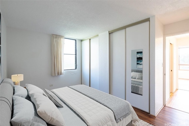 bedroom with multiple windows, two closets, a textured ceiling, and wood finished floors