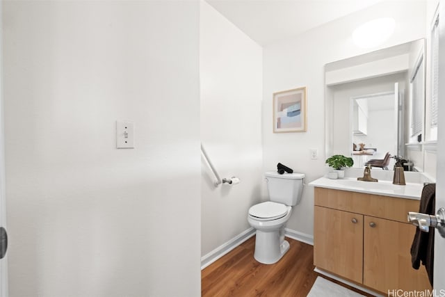 half bath featuring toilet, vanity, baseboards, and wood finished floors