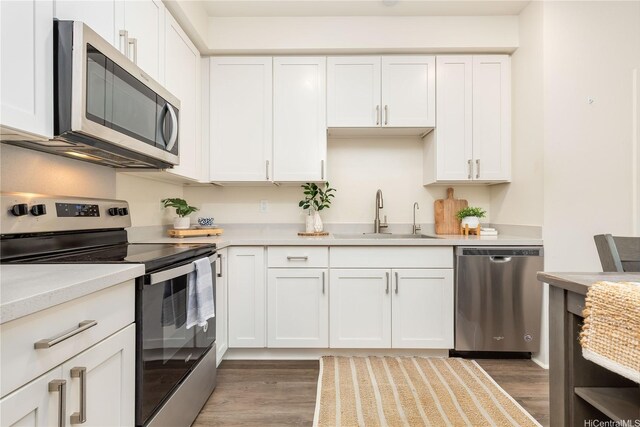 kitchen featuring wood finished floors, a sink, stainless steel appliances, light countertops, and white cabinets