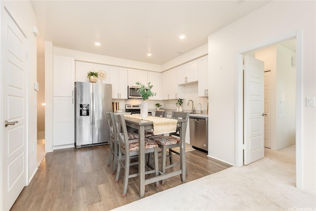kitchen with white cabinets, stainless steel appliances, recessed lighting, wood finished floors, and light countertops