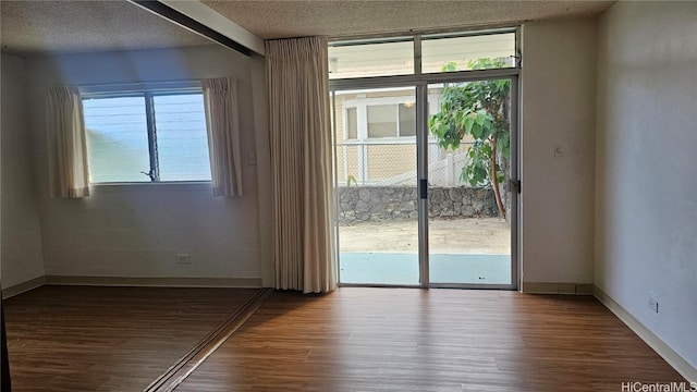 unfurnished room with a wealth of natural light, a textured ceiling, baseboards, and wood finished floors