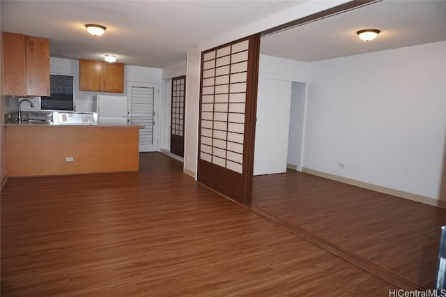 kitchen featuring brown cabinets, a sink, dark wood-style floors, freestanding refrigerator, and a peninsula