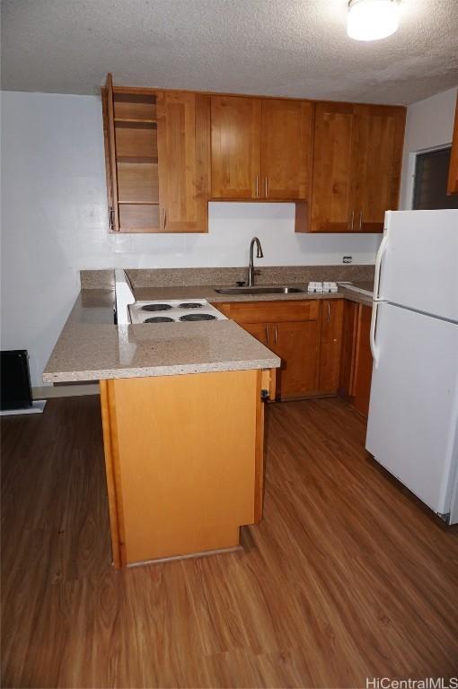 kitchen featuring a peninsula, freestanding refrigerator, wood finished floors, brown cabinetry, and a sink