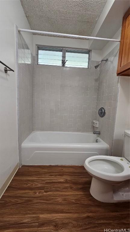 full bathroom with a textured ceiling, toilet,  shower combination, and wood finished floors