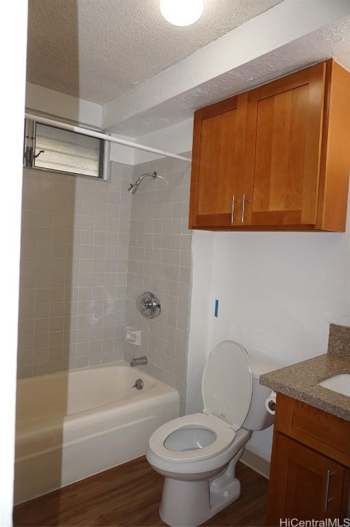 bathroom with vanity, a textured ceiling, wood finished floors, shower / bath combination, and toilet