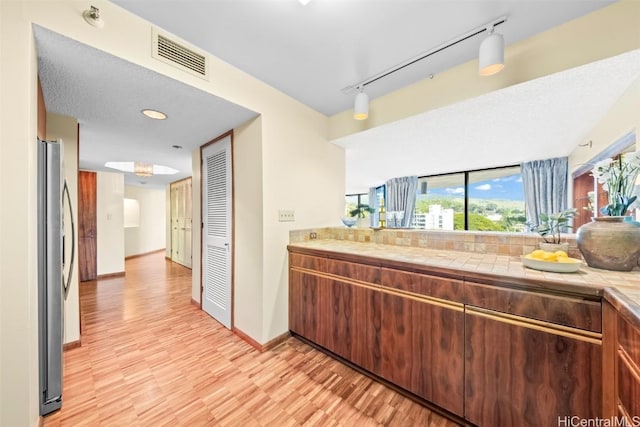 kitchen featuring visible vents, backsplash, baseboards, light wood-type flooring, and freestanding refrigerator