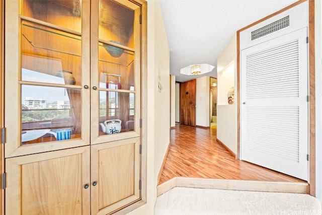 hallway with light wood-type flooring, visible vents, and baseboards