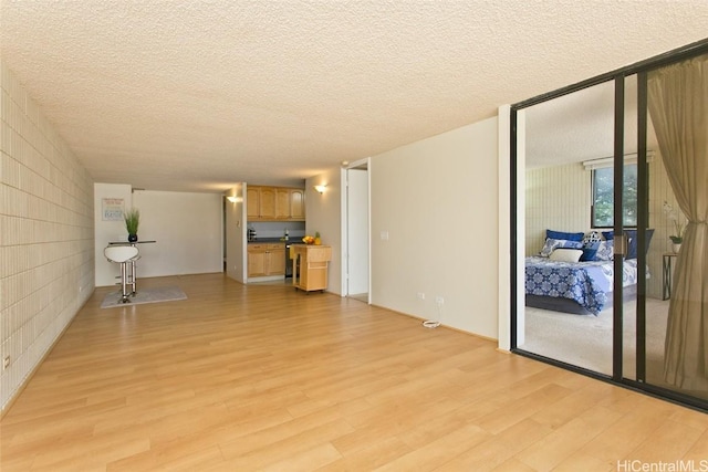 unfurnished living room with floor to ceiling windows, concrete block wall, light wood-type flooring, and a textured ceiling