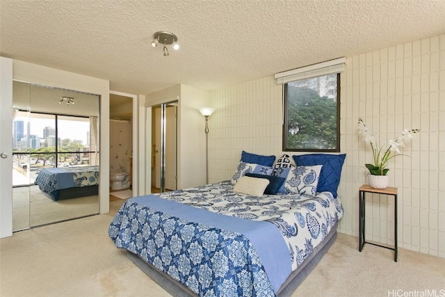 carpeted bedroom with a closet, connected bathroom, a textured ceiling, and tile walls