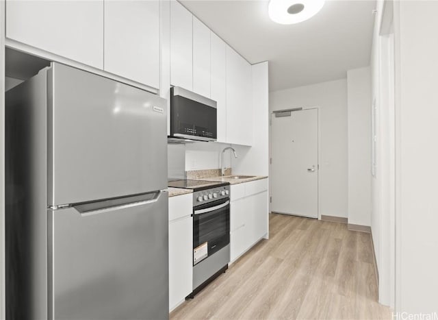 kitchen featuring light countertops, light wood-style floors, white cabinets, stainless steel appliances, and a sink