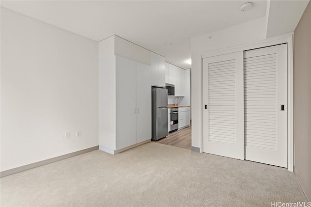 unfurnished bedroom with light carpet, freestanding refrigerator, and a sink