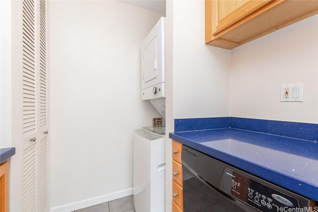 clothes washing area with light tile patterned floors, cabinet space, stacked washing maching and dryer, and baseboards