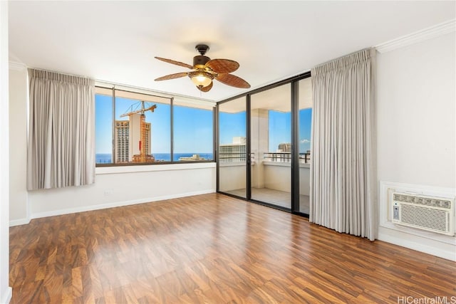 unfurnished room with a city view, wood finished floors, a wall unit AC, baseboards, and ceiling fan