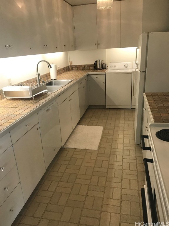 kitchen featuring white appliances, a sink, brick patterned floor, white cabinetry, and washer and clothes dryer