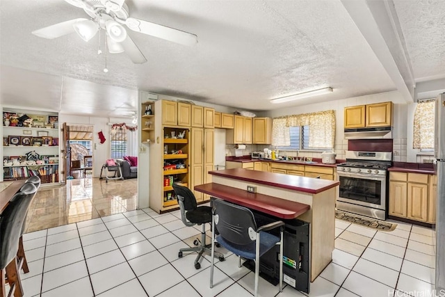 kitchen featuring under cabinet range hood, light tile patterned floors, gas range, and dark countertops