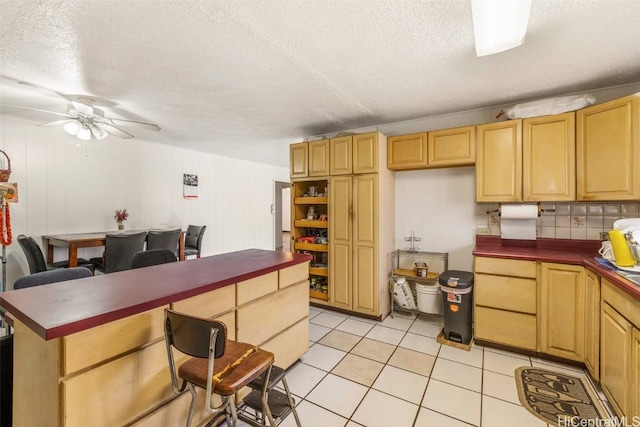 kitchen featuring a kitchen bar, a ceiling fan, dark countertops, a textured ceiling, and light tile patterned floors