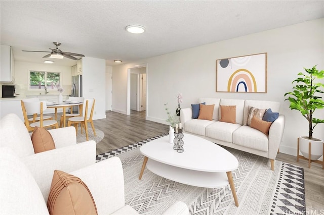 living area featuring baseboards, a textured ceiling, light wood-style flooring, and a ceiling fan