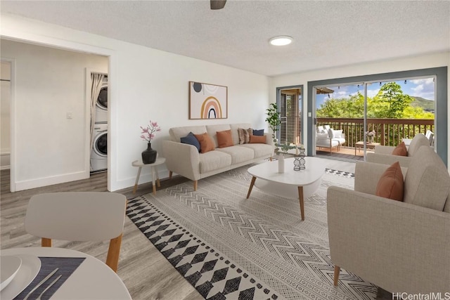 living area with baseboards, a textured ceiling, wood finished floors, and stacked washing maching and dryer