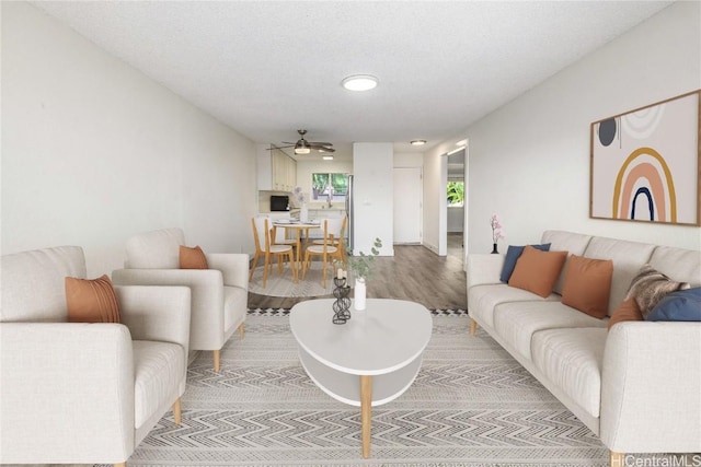 living room featuring light wood finished floors, a textured ceiling, and ceiling fan