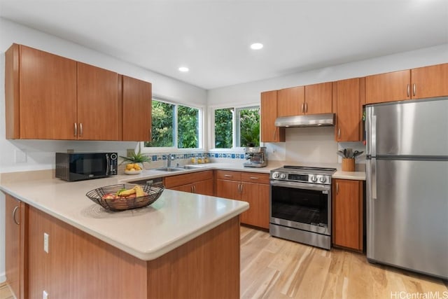 kitchen with under cabinet range hood, light countertops, a peninsula, stainless steel appliances, and a sink